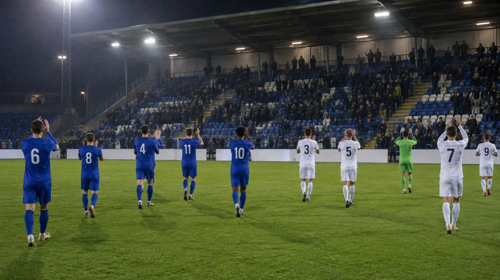 Spelare applåderar publiken efter slutsignalen på en stadion i kvällsljus