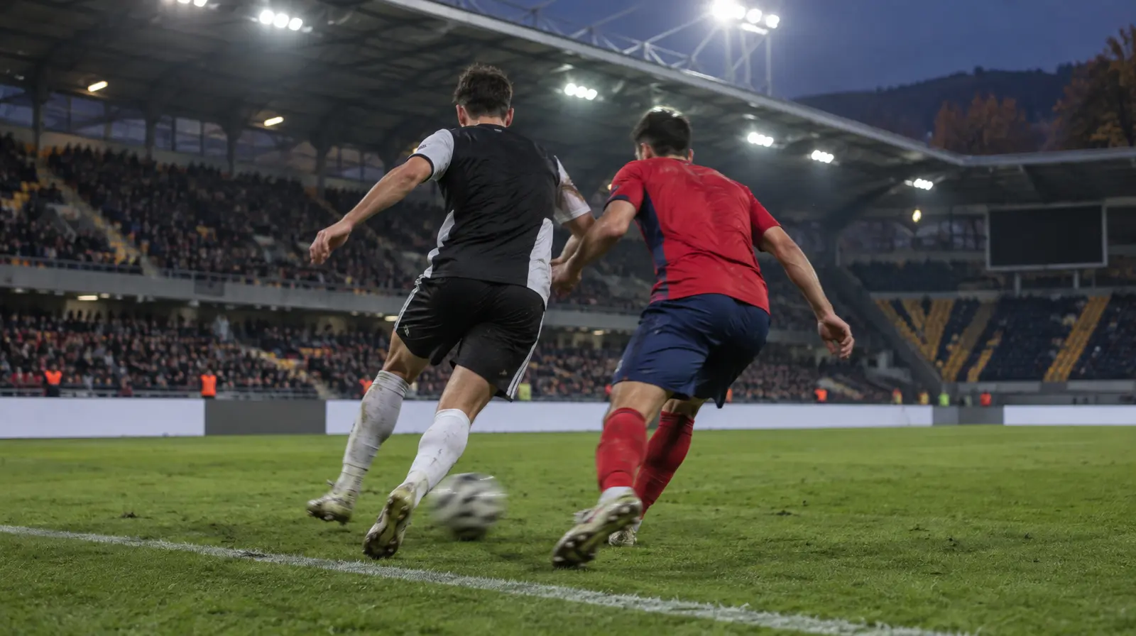 Två spelare kämpar om bollen vid sidlinjen i kvällsljus